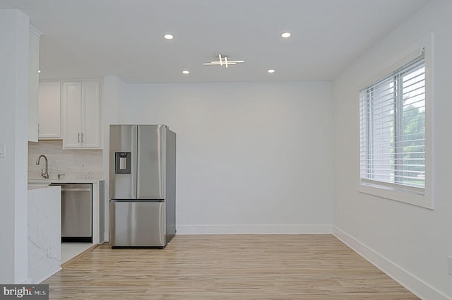 kitchen with appliances with stainless steel finishes, light stone countertops, light hardwood / wood-style flooring, and white cabinets