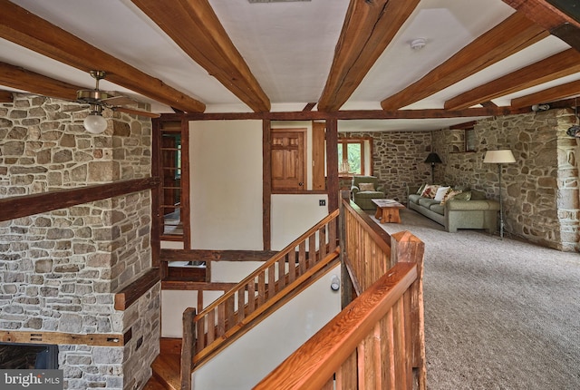 interior space with a stone fireplace, carpet flooring, ceiling fan, and beamed ceiling