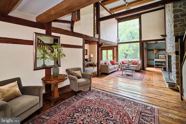 living room with wood-type flooring, beamed ceiling, a fireplace, and a towering ceiling