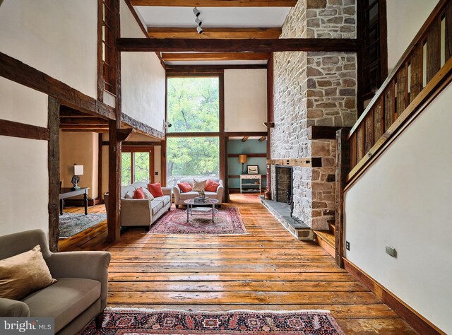 living room featuring wood-type flooring, a stone fireplace, beam ceiling, and a towering ceiling