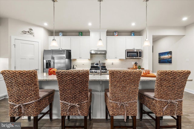 kitchen featuring pendant lighting, a kitchen island with sink, dark wood-type flooring, stainless steel appliances, and a breakfast bar area