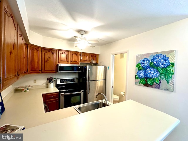 kitchen featuring sink, kitchen peninsula, stainless steel appliances, backsplash, and ceiling fan