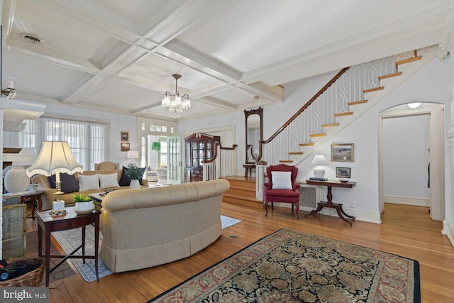 living room featuring beam ceiling, coffered ceiling, a chandelier, hardwood / wood-style flooring, and ornamental molding