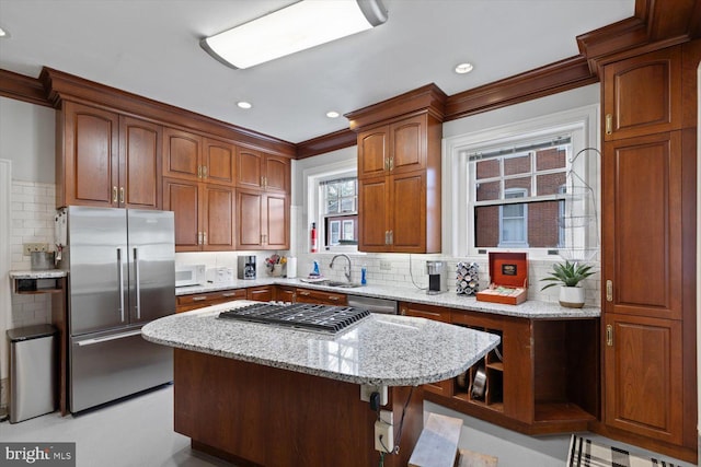 kitchen featuring appliances with stainless steel finishes, backsplash, light stone counters, sink, and a kitchen island