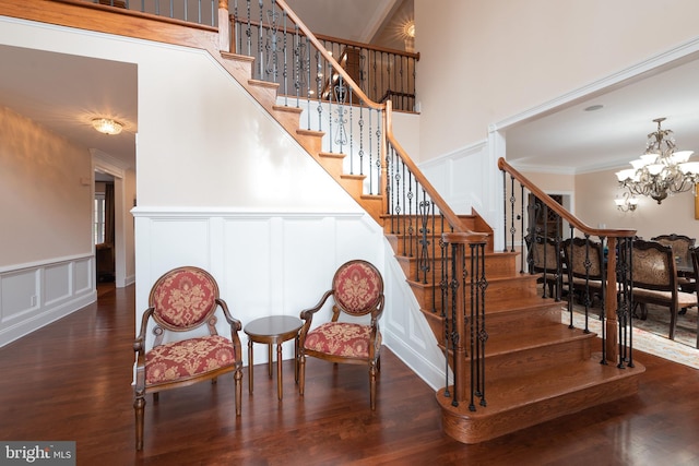 staircase featuring wood-type flooring, an inviting chandelier, ornamental molding, and a high ceiling