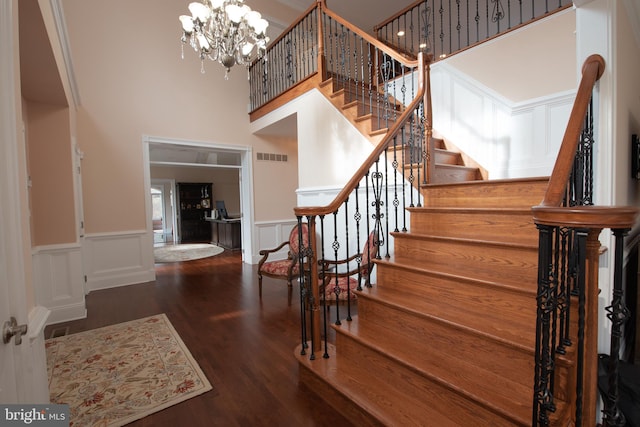 stairway with wood-type flooring, a towering ceiling, and a chandelier