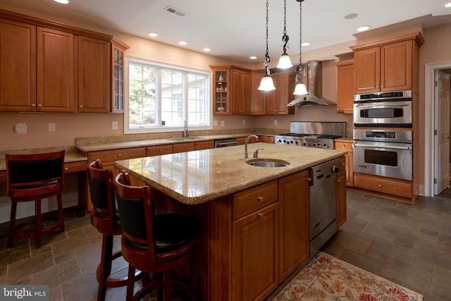 kitchen with appliances with stainless steel finishes, a center island with sink, wall chimney exhaust hood, and sink