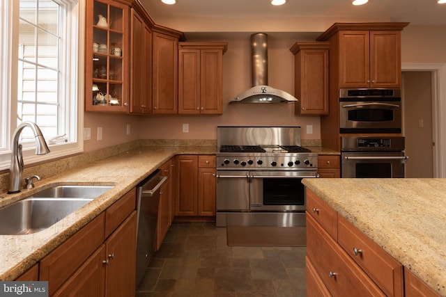 kitchen with light stone countertops, appliances with stainless steel finishes, sink, and wall chimney range hood