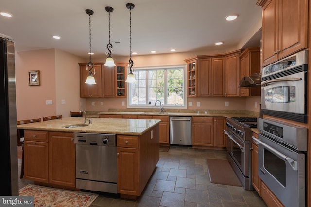 kitchen with appliances with stainless steel finishes, light stone counters, a kitchen island with sink, sink, and pendant lighting