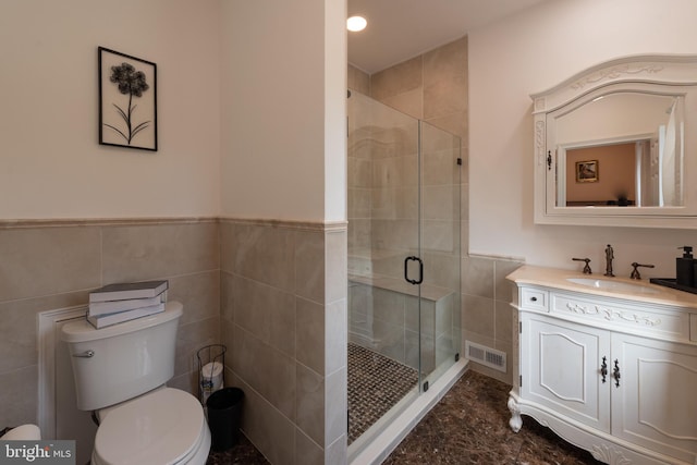 bathroom with vanity, toilet, a shower with shower door, and tile walls