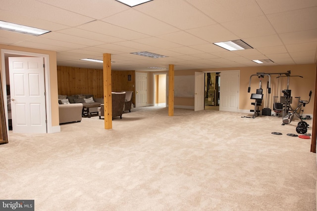 workout room with a paneled ceiling, wooden walls, and light colored carpet