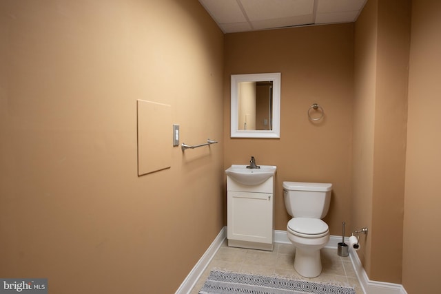 bathroom with tile patterned flooring, vanity, toilet, and a drop ceiling