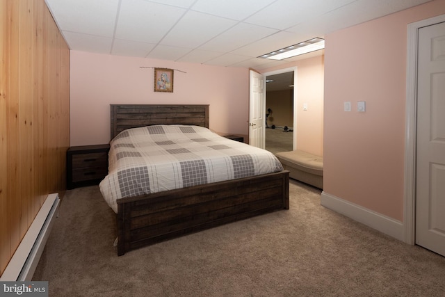 carpeted bedroom with a baseboard radiator, a drop ceiling, and wood walls