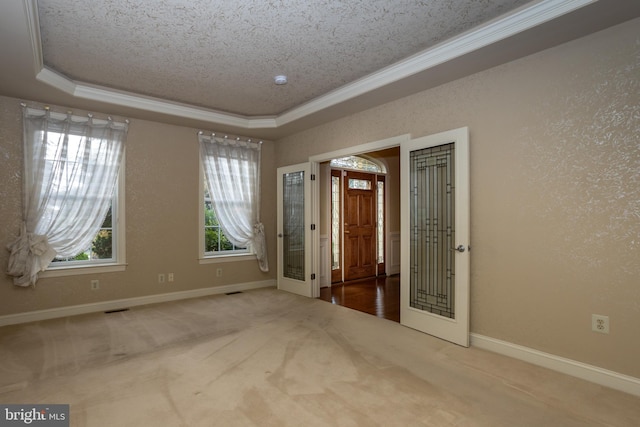 empty room with a textured ceiling, carpet flooring, ornamental molding, and a tray ceiling