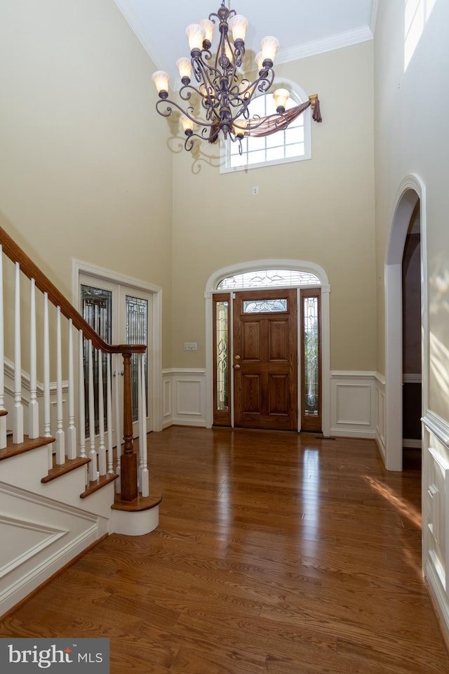 foyer entrance featuring an inviting chandelier, a high ceiling, dark hardwood / wood-style floors, and crown molding