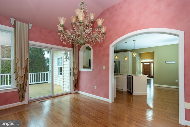 unfurnished room with a notable chandelier, wine cooler, vaulted ceiling, and hardwood / wood-style flooring