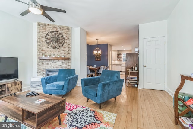 living room with ceiling fan with notable chandelier, a brick fireplace, and light hardwood / wood-style flooring