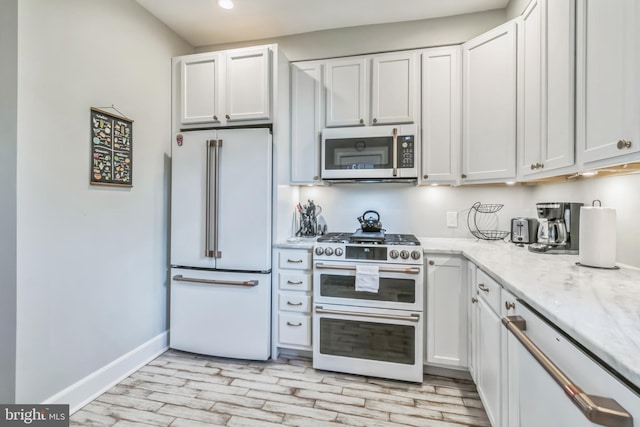 kitchen featuring white cabinets, light wood-type flooring, premium appliances, and light stone countertops