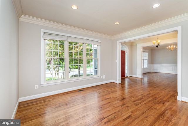 empty room featuring wood-type flooring, decorative columns, crown molding, and a chandelier