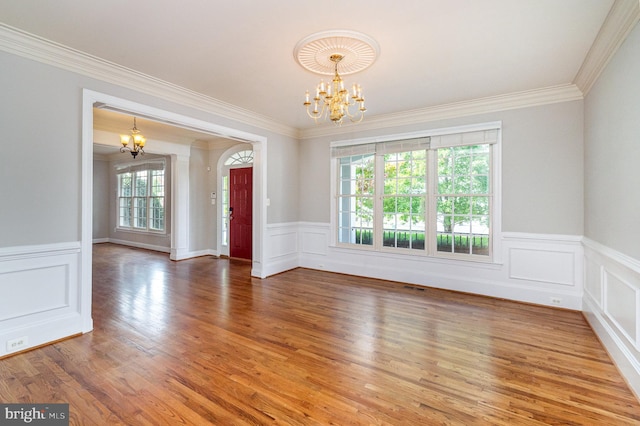 spare room featuring hardwood / wood-style flooring, ornamental molding, an inviting chandelier, and plenty of natural light