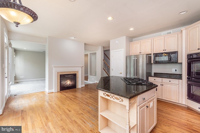 kitchen featuring light wood-type flooring, a tiled fireplace, a kitchen island, black appliances, and dark stone countertops