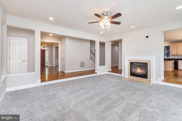 unfurnished living room with carpet floors, ceiling fan with notable chandelier, and a fireplace