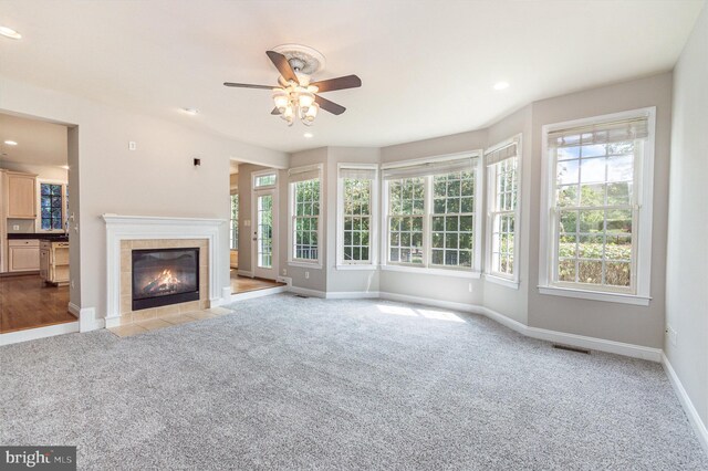 unfurnished living room with ceiling fan, light colored carpet, a fireplace, and a wealth of natural light