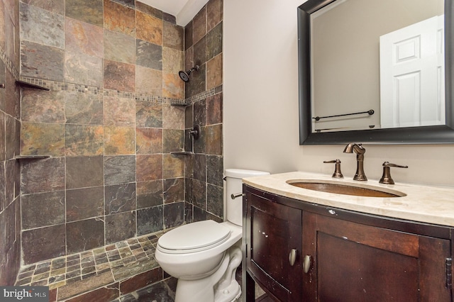 bathroom with tiled shower, vanity, and toilet