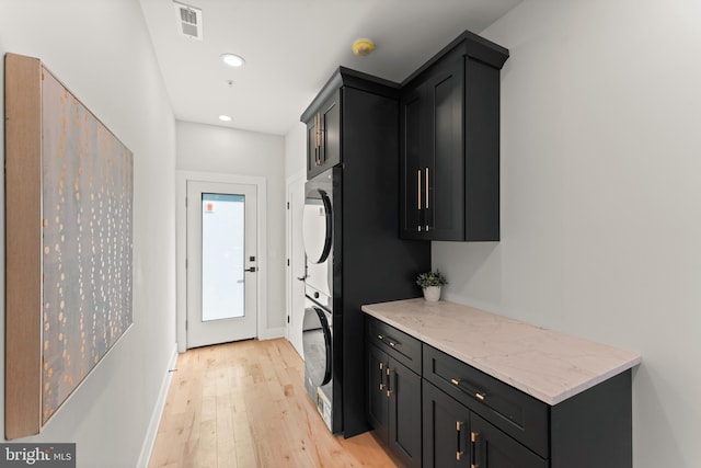 laundry room featuring stacked washer / drying machine, light wood-type flooring, and cabinets