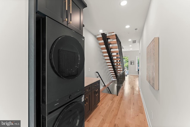 laundry area featuring cabinets, light hardwood / wood-style floors, and stacked washer / dryer