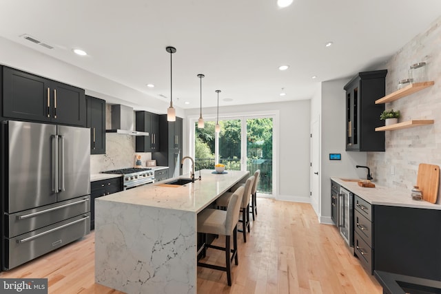 kitchen with hanging light fixtures, high end appliances, light stone countertops, a kitchen bar, and wall chimney range hood