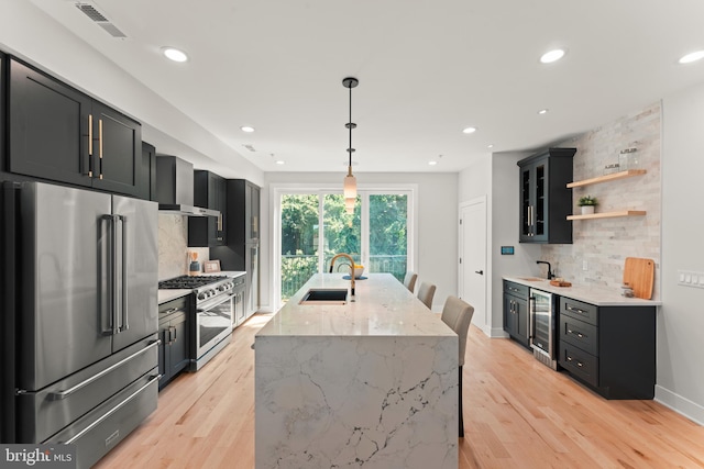 kitchen with light stone counters, wine cooler, light wood-type flooring, high quality appliances, and sink