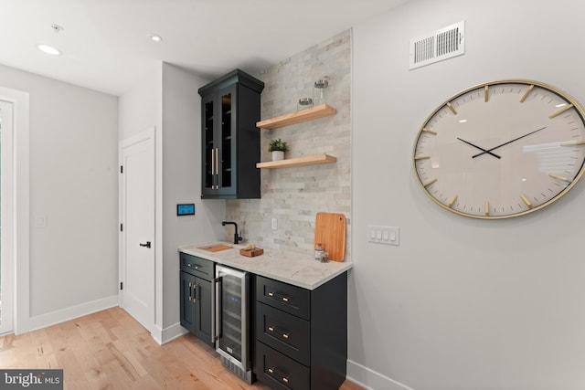 bar with beverage cooler, light wood-type flooring, sink, and tasteful backsplash