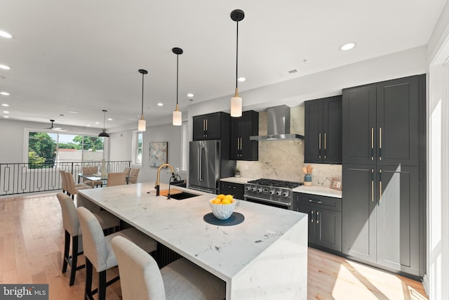 kitchen with sink, wall chimney range hood, premium appliances, light stone countertops, and a spacious island