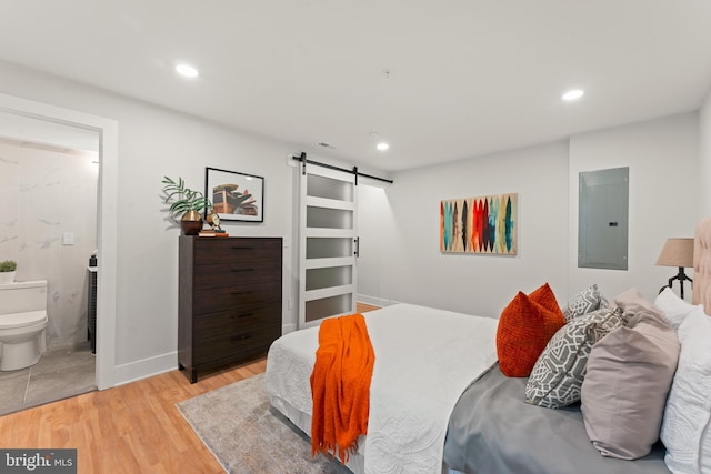 bedroom with a barn door, light hardwood / wood-style floors, electric panel, and ensuite bath