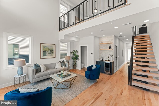 living room featuring wine cooler, light wood-type flooring, bar, and a high ceiling