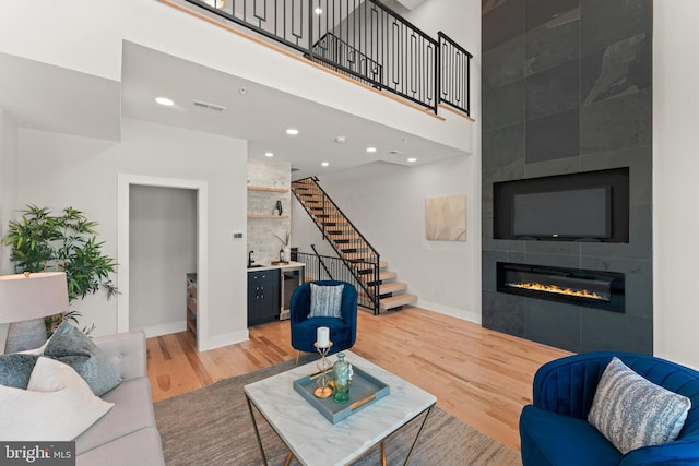 living room featuring wood-type flooring, wine cooler, a towering ceiling, and a tile fireplace