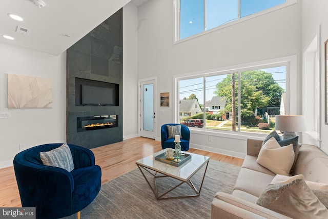 living room with a tile fireplace, a towering ceiling, wood-type flooring, and plenty of natural light