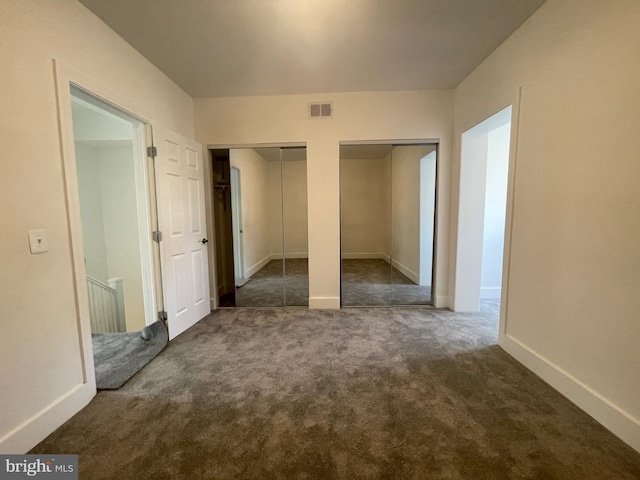 unfurnished bedroom featuring dark carpet and multiple closets