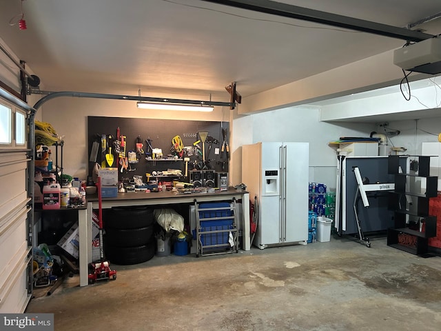 garage featuring a garage door opener, a workshop area, and white refrigerator with ice dispenser