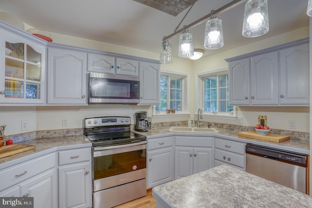 kitchen featuring sink, decorative light fixtures, white cabinetry, appliances with stainless steel finishes, and light wood-type flooring