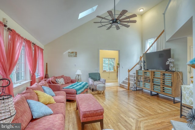 living room featuring high vaulted ceiling, a skylight, light hardwood / wood-style flooring, and ceiling fan