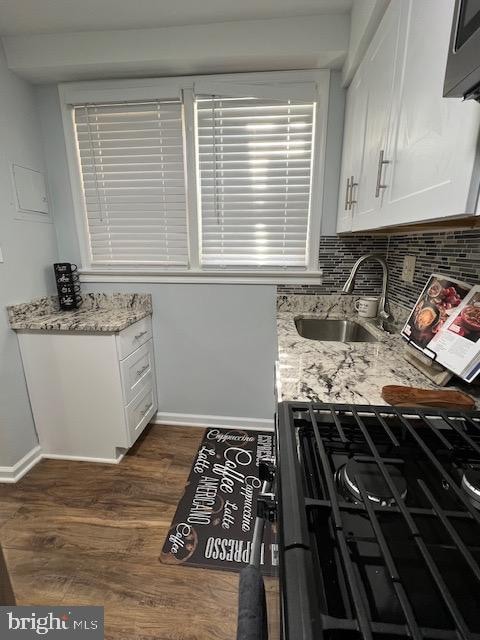 kitchen with light stone counters, white cabinetry, black appliances, dark wood-type flooring, and sink