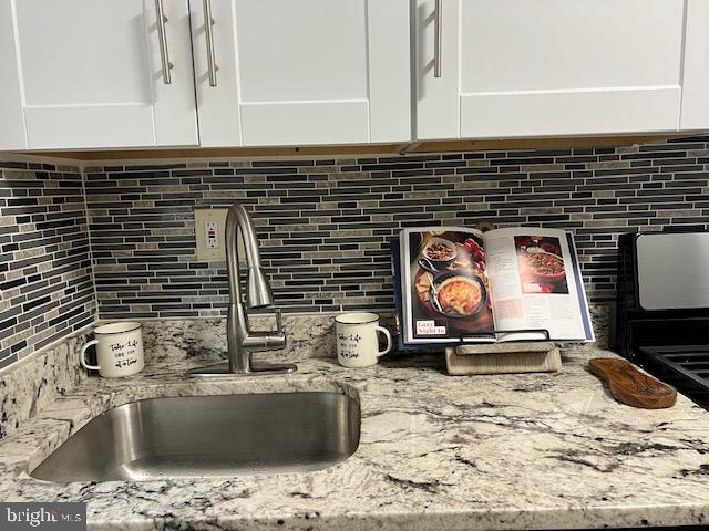 interior details with backsplash, sink, light stone counters, and white cabinets