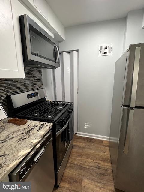 kitchen with tasteful backsplash, stainless steel appliances, white cabinets, dark wood-type flooring, and light stone counters