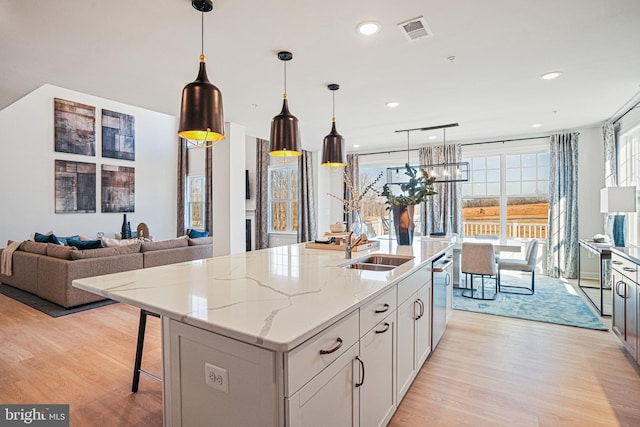 kitchen with light stone counters, sink, pendant lighting, a center island with sink, and light hardwood / wood-style floors