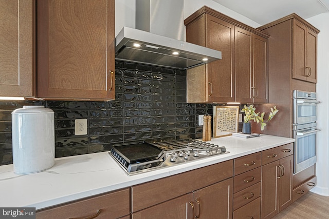 kitchen with appliances with stainless steel finishes, backsplash, light hardwood / wood-style flooring, and wall chimney exhaust hood