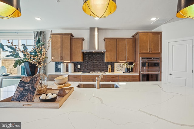 kitchen featuring backsplash, sink, wall chimney exhaust hood, light stone counters, and stainless steel appliances