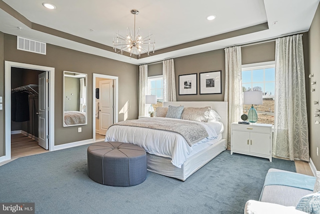 carpeted bedroom with a walk in closet, a tray ceiling, an inviting chandelier, and multiple windows