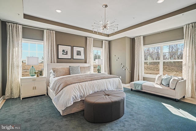 bedroom with dark colored carpet, a tray ceiling, and multiple windows